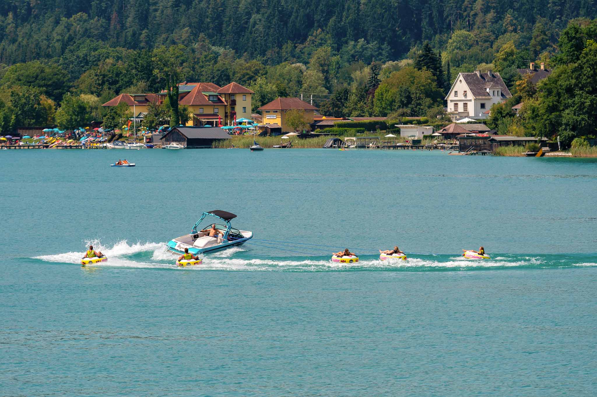 WORTHERSEE, AUSTRIA Happy young people, on inflatable attractions, drive behind a motorboat on the lake.